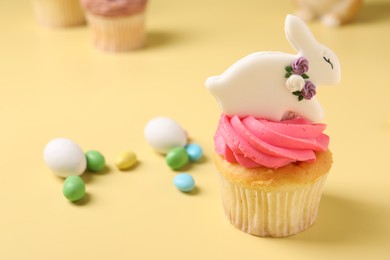 Tasty cupcake with Easter decor on pale yellow background, closeup