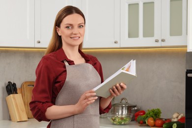 Happy woman with recipe book in kitchen, space for text