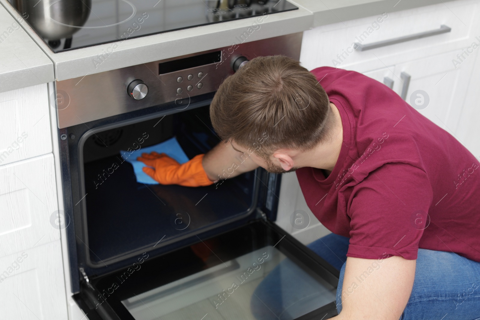 Photo of Young man cleaning oven with rag in kitchen