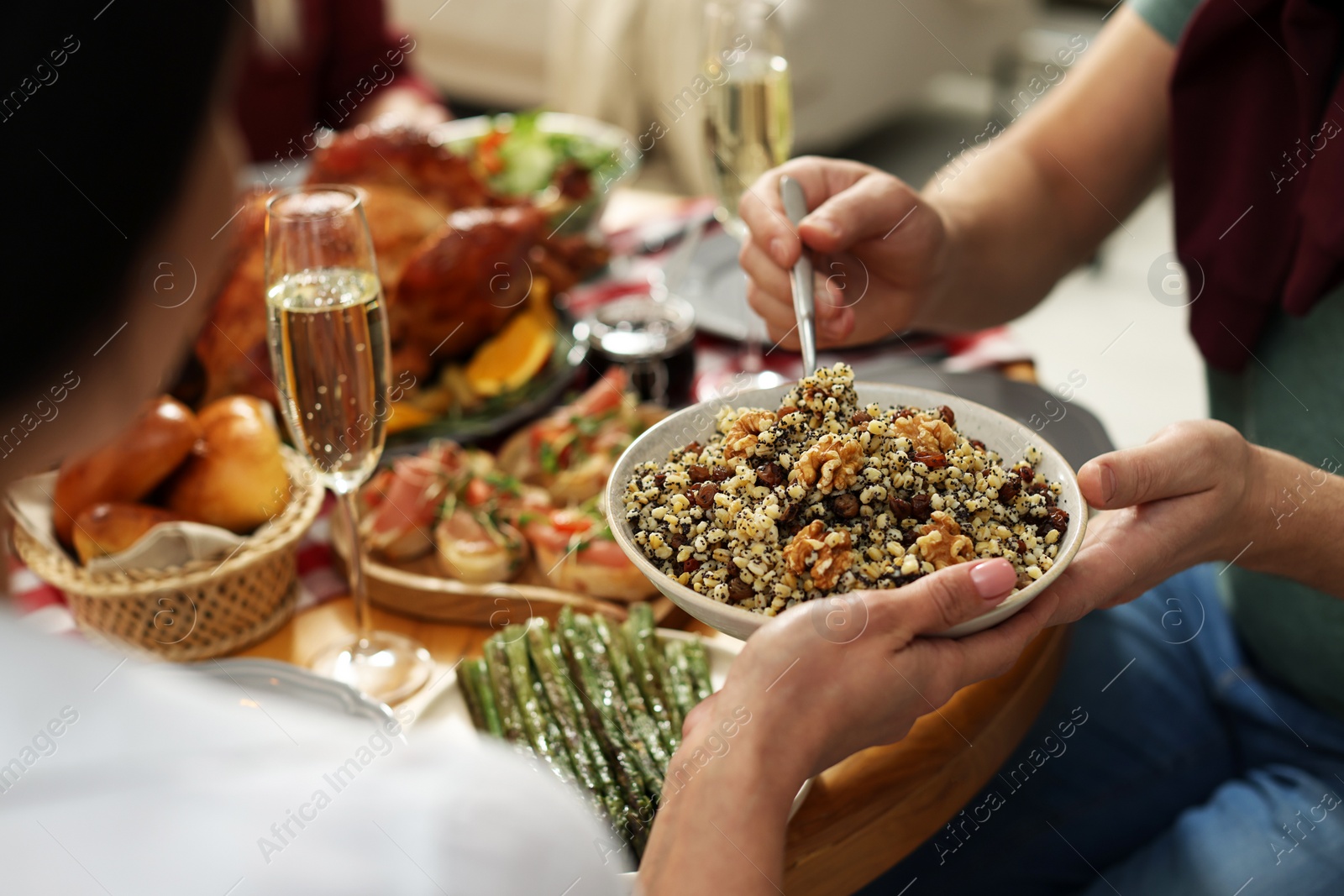 Photo of Woman giving bowl of traditional Christmas Slavic dish kutia to man at festive dinner, closeup