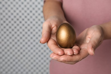 Woman holding golden egg on light background, closeup. Space for text