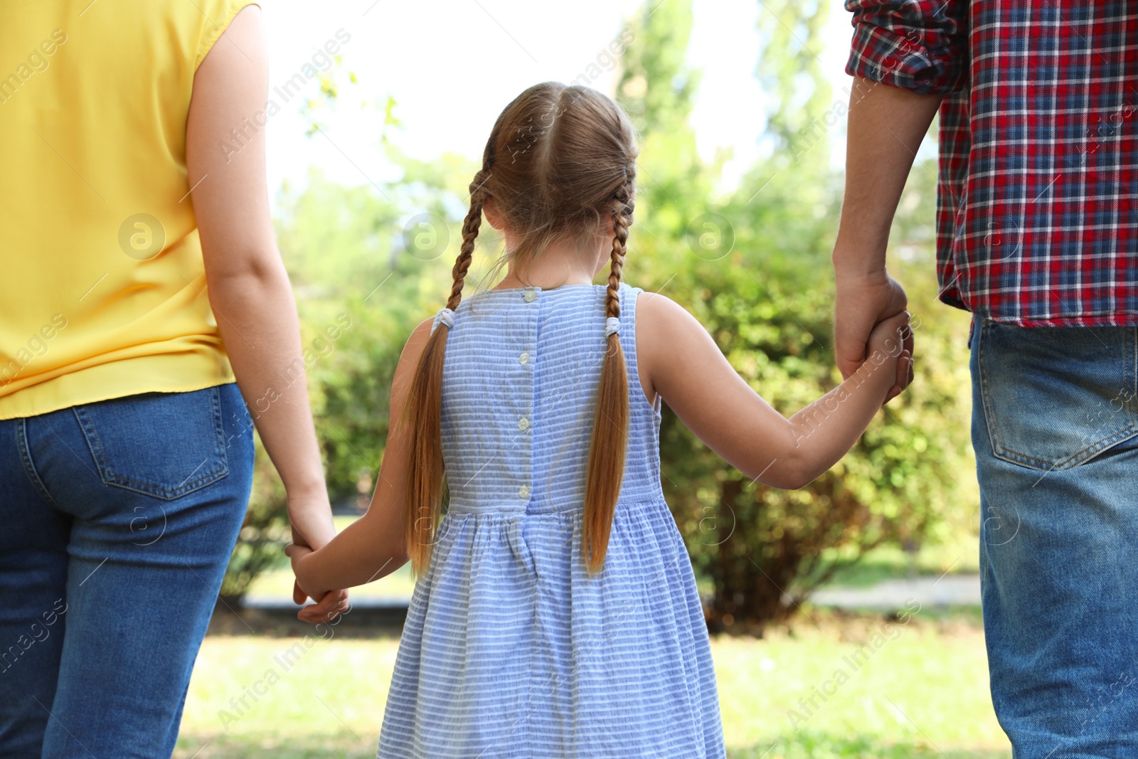 Photo of Little girl and her parents holding hands outdoors. Family weekend