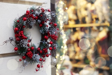 Photo of Beautiful Christmas wreath hanging on white building wall outdoors, space for text