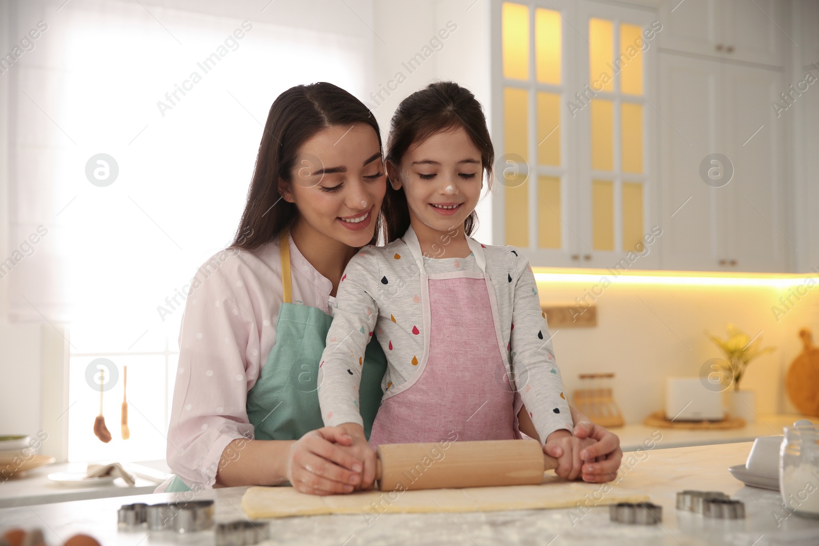 Photo of Mother with her cute little daughter rolling dough in kitchen