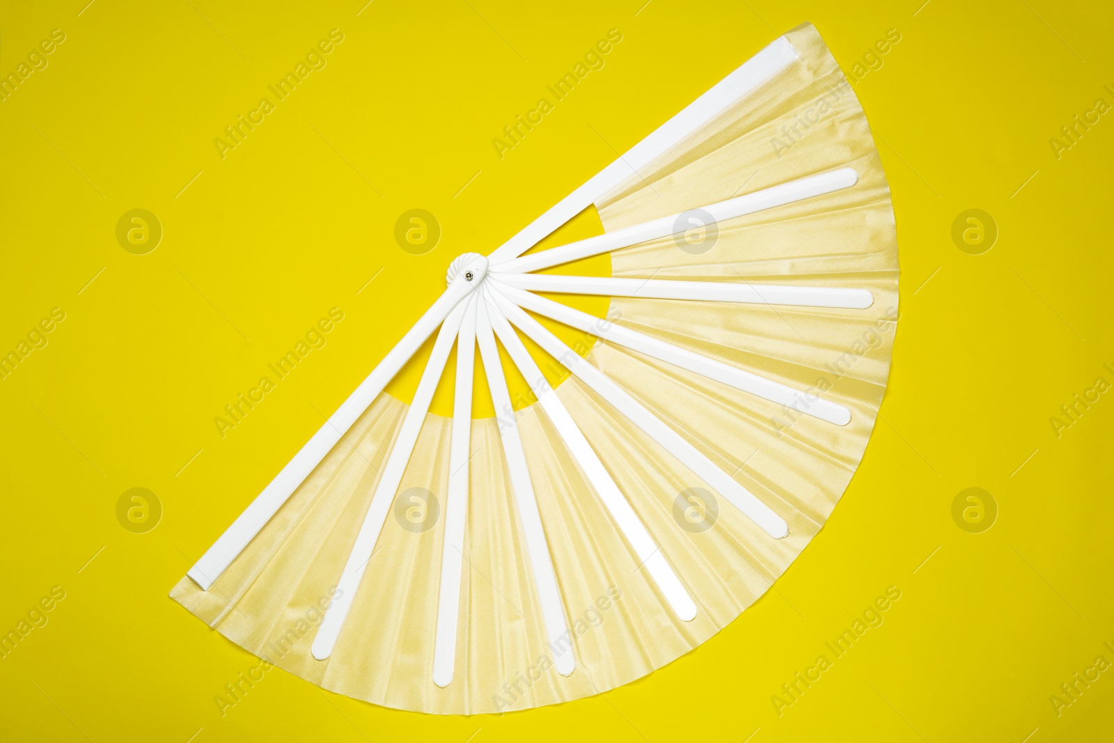 Photo of White hand fan on yellow background, top view