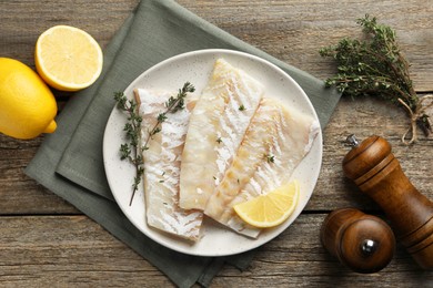 Photo of Fresh raw cod fillets with thyme and lemon on wooden table, flat lay
