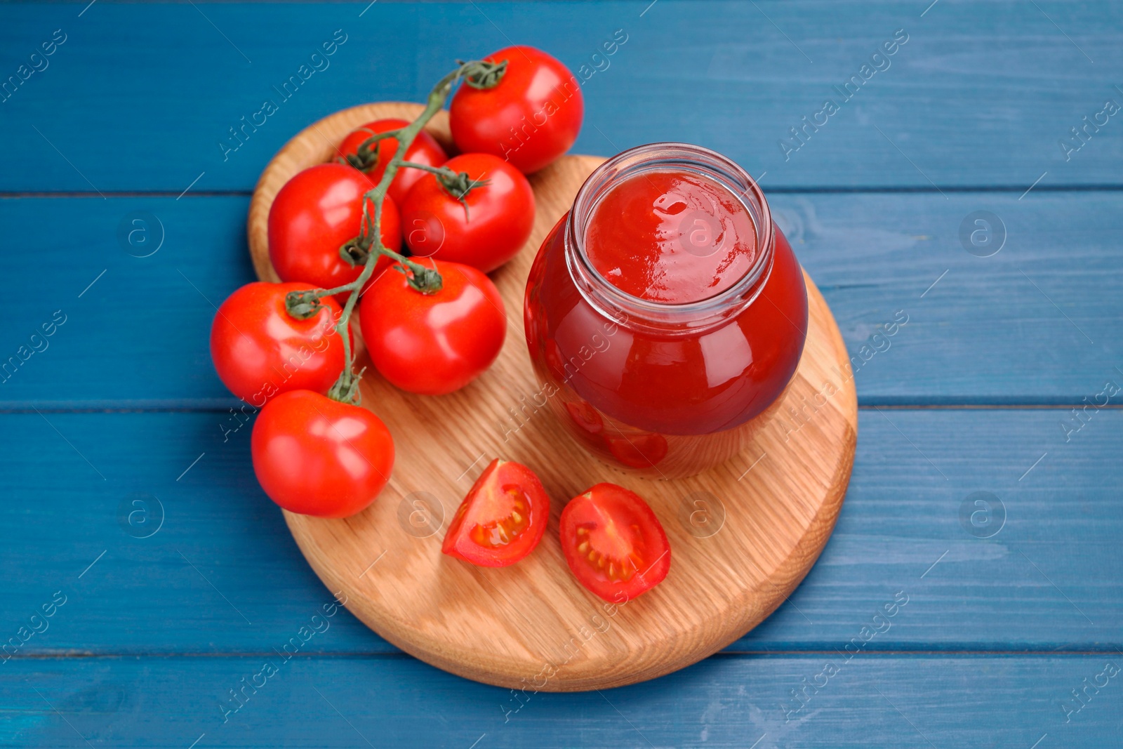 Photo of Organic ketchup in jar and fresh tomatoes on blue wooden table. Tomato sauce