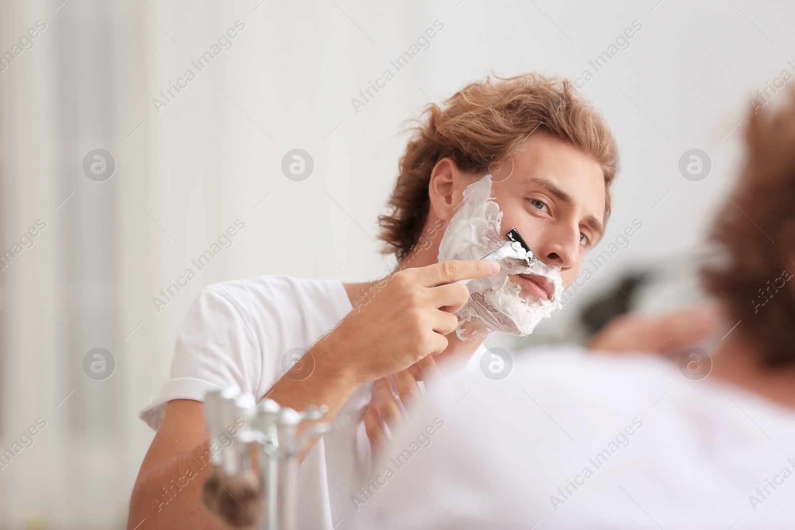 Photo of Young handsome man shaving in bathroom