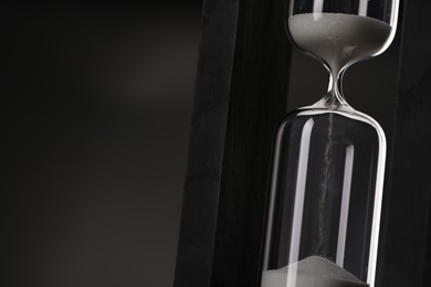 Photo of Hourglass with flowing sand on black background, closeup. Space for text