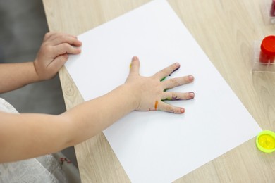 Photo of Little girl painting with palm at wooden table, closeup