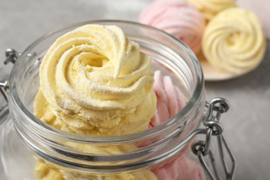 Photo of Yellow and pink delicious marshmallows in glass jar on table, closeup