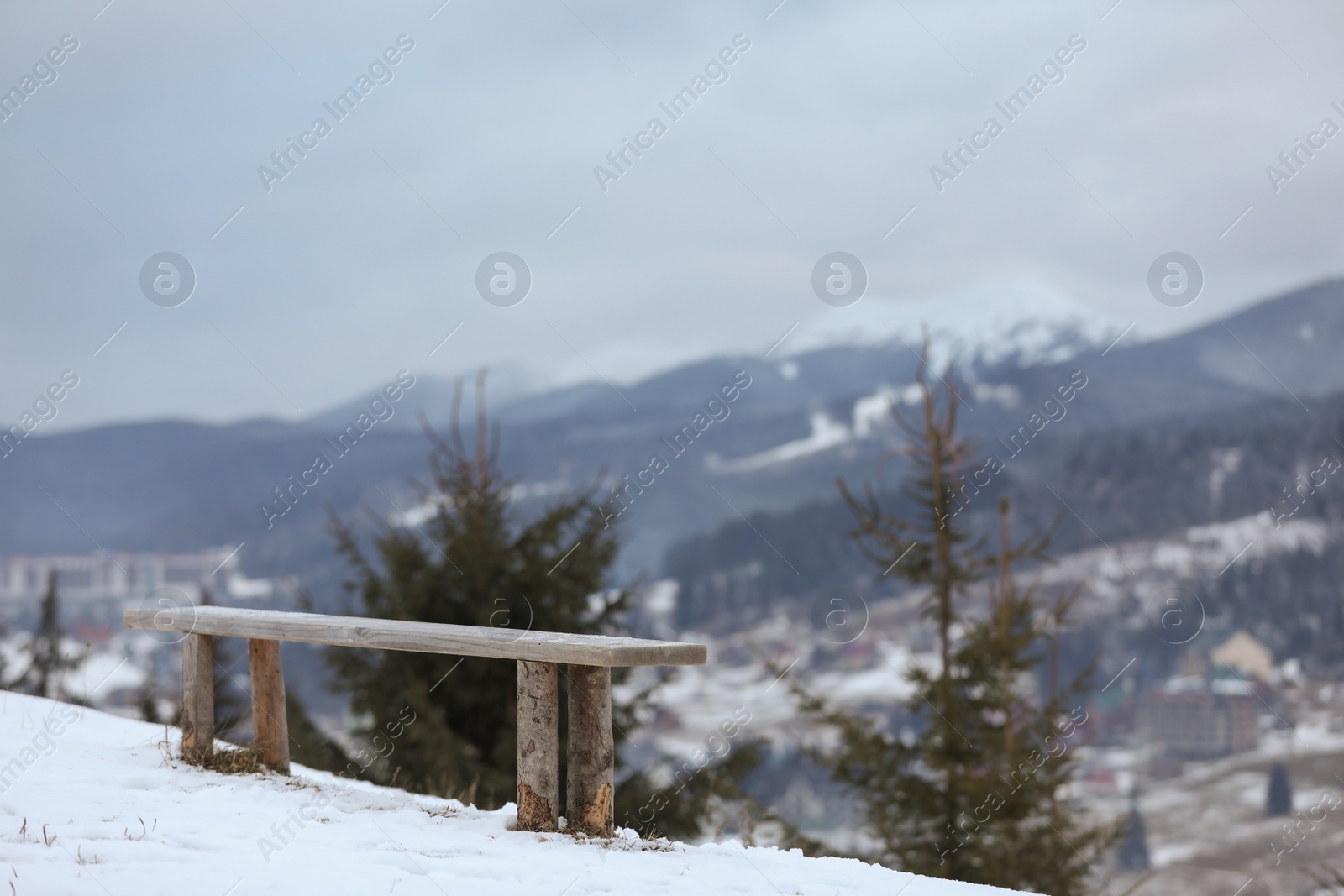 Photo of Beautiful winter landscape with bench on snowy hill over mountain village near forest