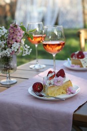 Photo of Vase with spring flowers, wine and cake on table served for romantic date in garden