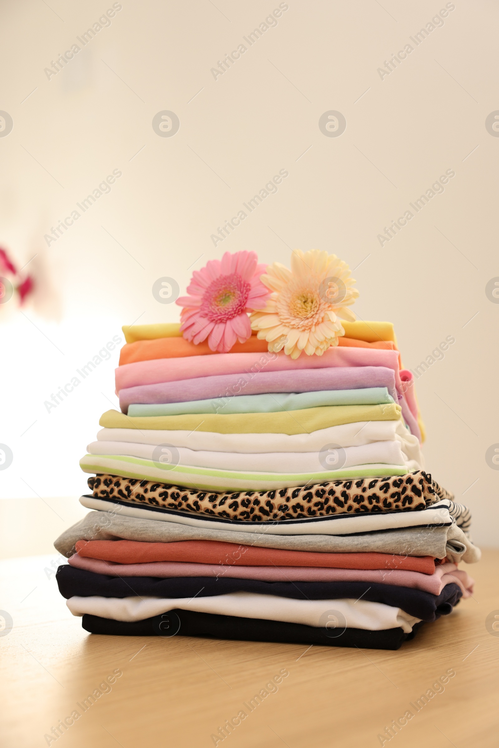 Photo of Stack of clean clothes and flowers on wooden table