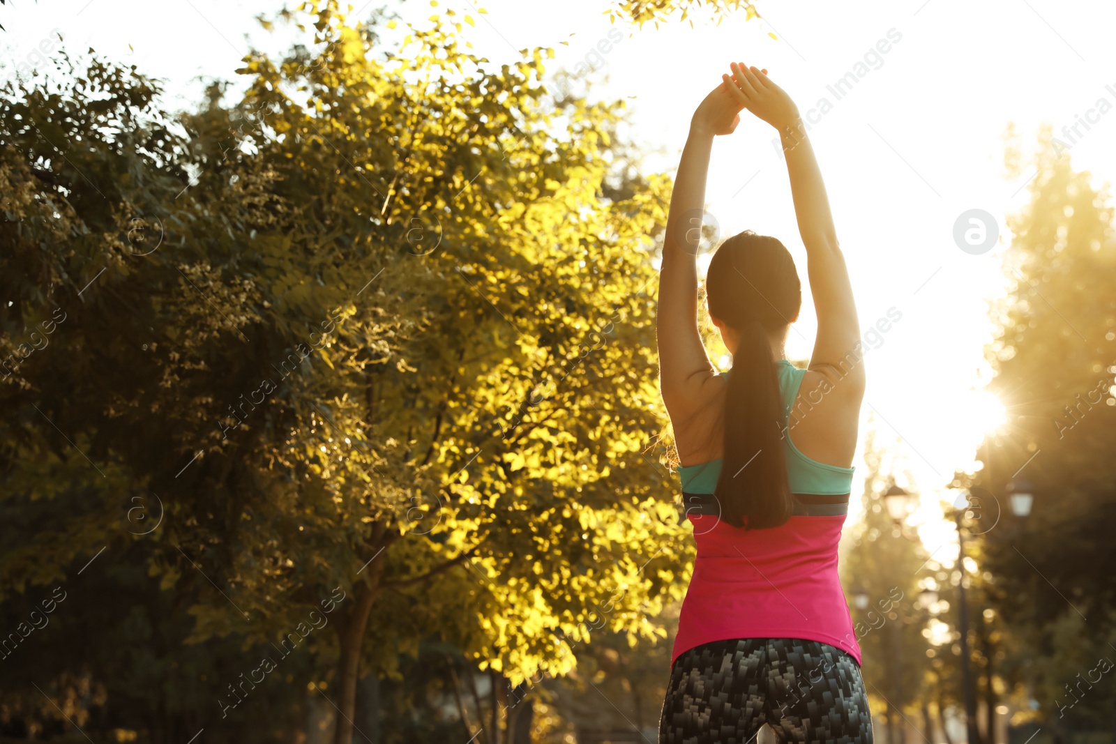 Photo of Young woman stretching before morning run in park, back view. Space for text