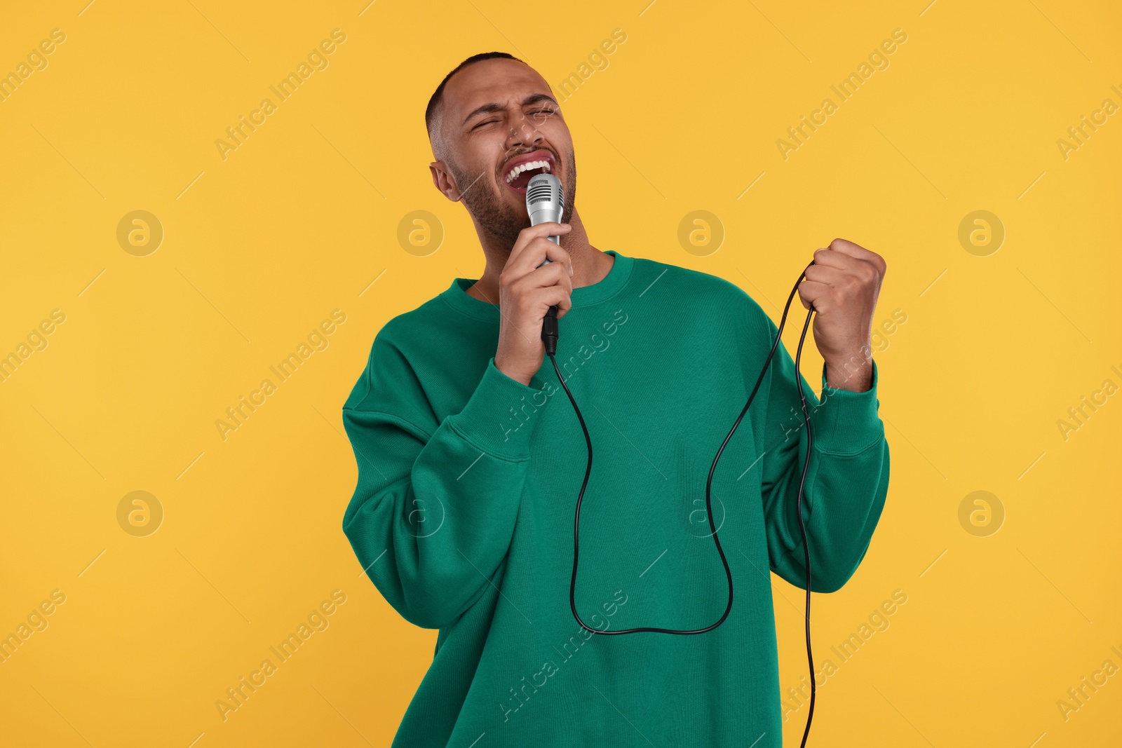 Photo of Handsome man with microphone singing on orange background