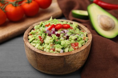 Bowl of delicious guacamole and ingredients on grey wooden table, closeup