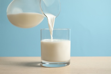 Photo of Pouring milk into glass on wooden table against light blue background