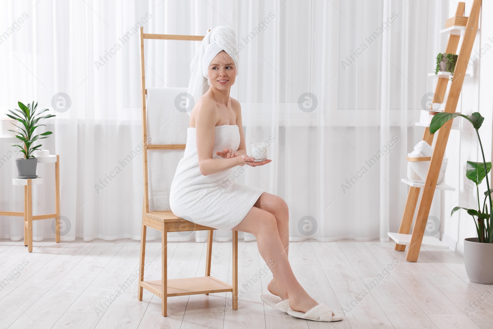 Photo of Beautiful young woman applying body cream onto arm indoors
