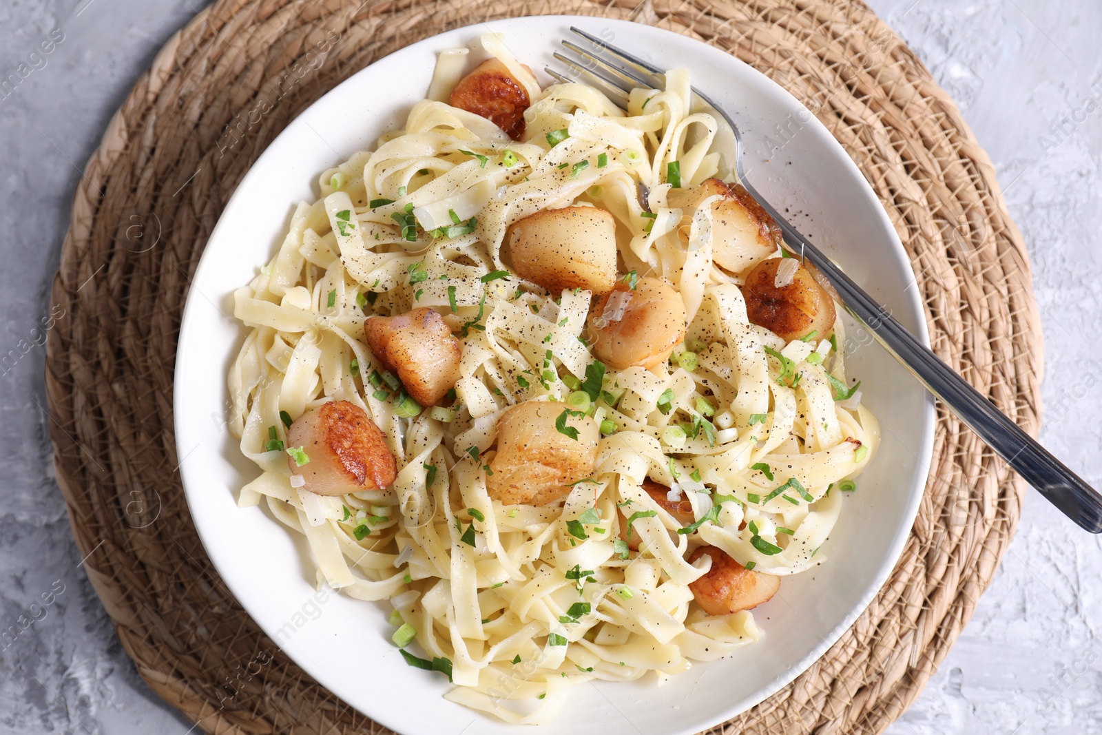 Photo of Delicious scallop pasta with spices in bowl on gray textured table, top view