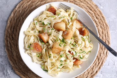 Photo of Delicious scallop pasta with spices in bowl on gray textured table, top view