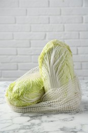 Fresh Chinese cabbages in string bag on white marble table near brick wall