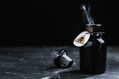 Photo of Open glass bottle of smoking poison with warning sign on black table. Space for text