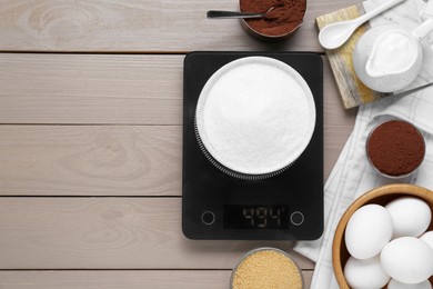 Electronic scales with sugar and different products on light wooden table, flat lay. Space for text