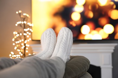 Photo of Woman wearing knitted socks in room decorated for Christmas, closeup