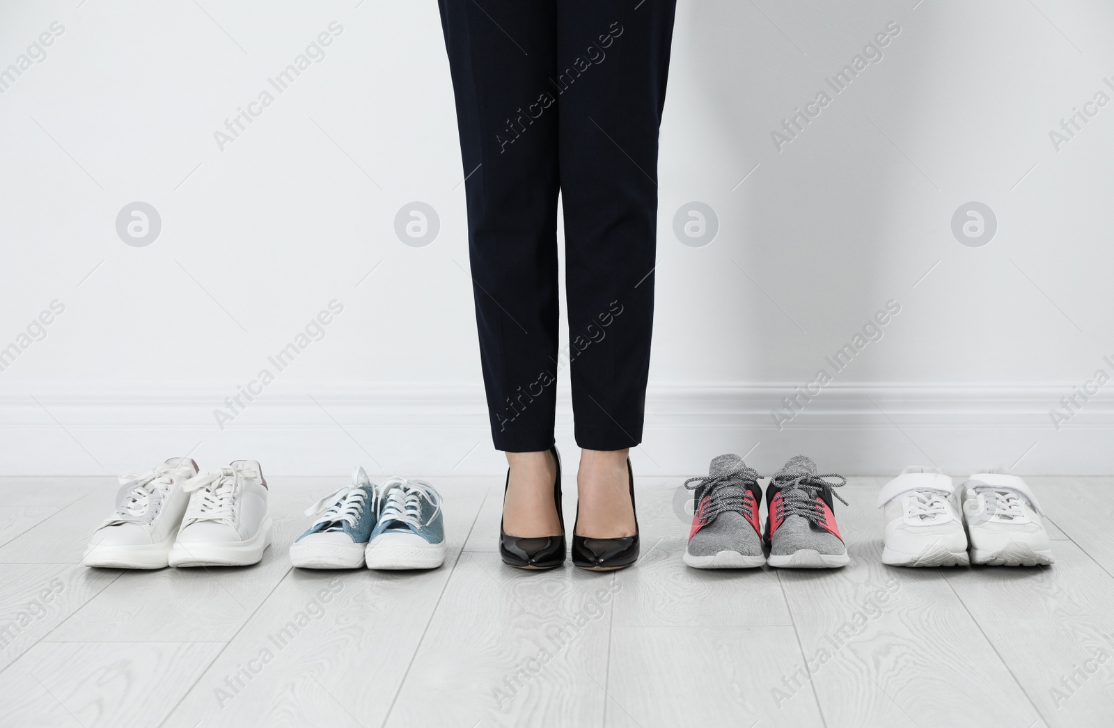 Photo of Different comfortable sneakers near businesswoman wearing high heel shoes indoors, closeup