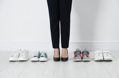 Photo of Different comfortable sneakers near businesswoman wearing high heel shoes indoors, closeup