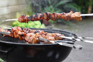 Photo of Cooking delicious kebab on metal skewers outdoors