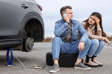 Photo of Young man calling to car service on roadside. Tire puncture