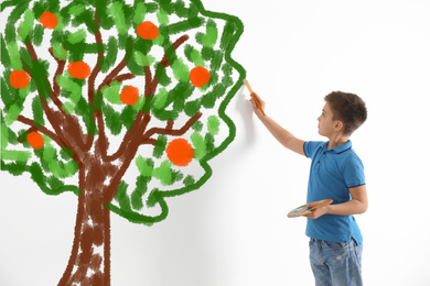 Cute child drawing tree on white wall indoors