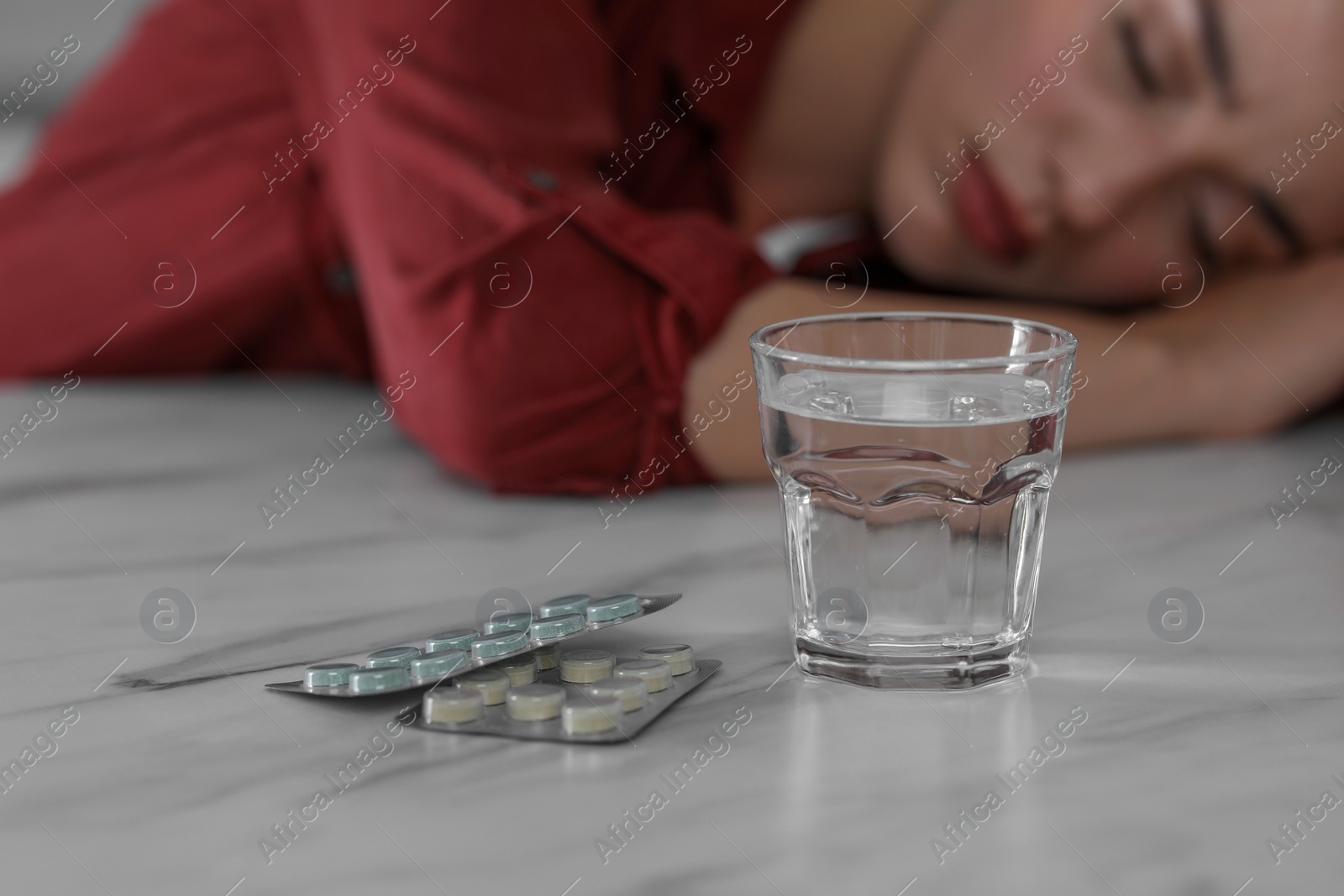Photo of Woman sleeping at white marble table, focus on blisters with antidepressant pills and glass of water