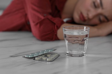 Photo of Woman sleeping at white marble table, focus on blisters with antidepressant pills and glass of water