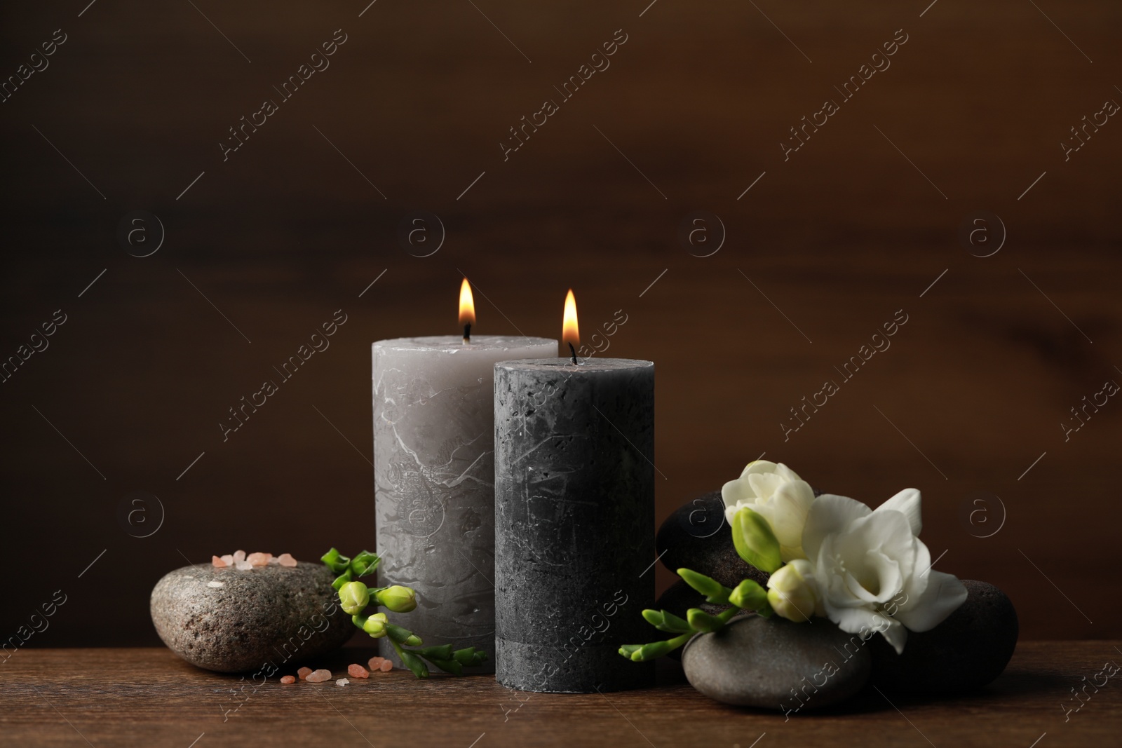 Photo of Beautiful composition with burning candles, spa stones and flowers on wooden table