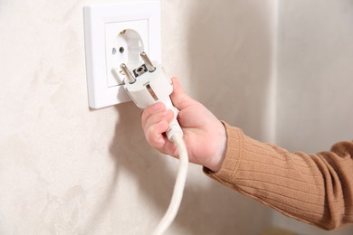 Little child playing with electrical socket and plug indoors, closeup. Dangerous situation