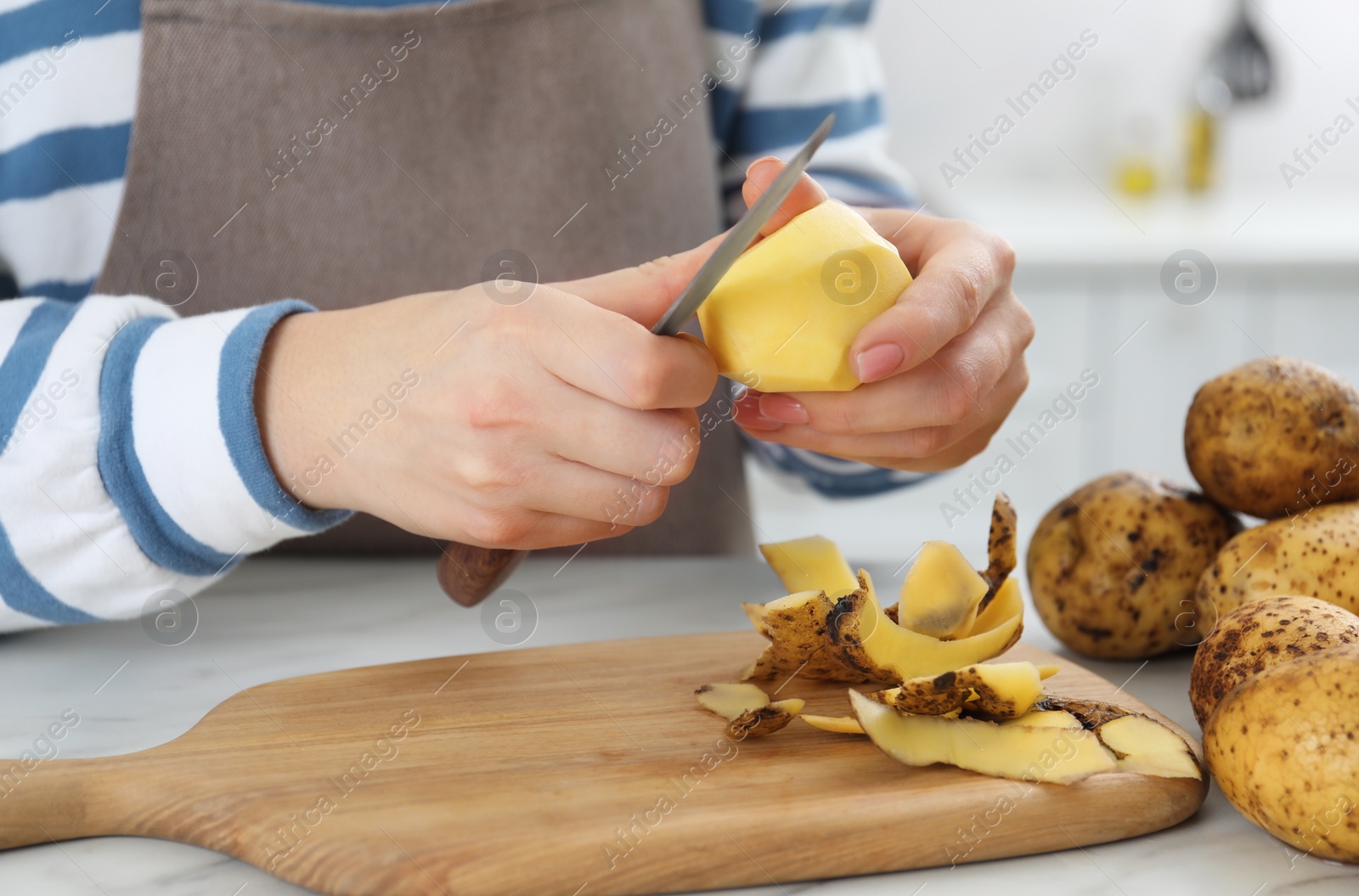 Photo of Woman peeling fresh potato with knife at white marble table indoors, closeup