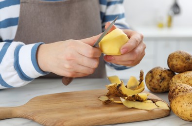 Photo of Woman peeling fresh potato with knife at white marble table indoors, closeup
