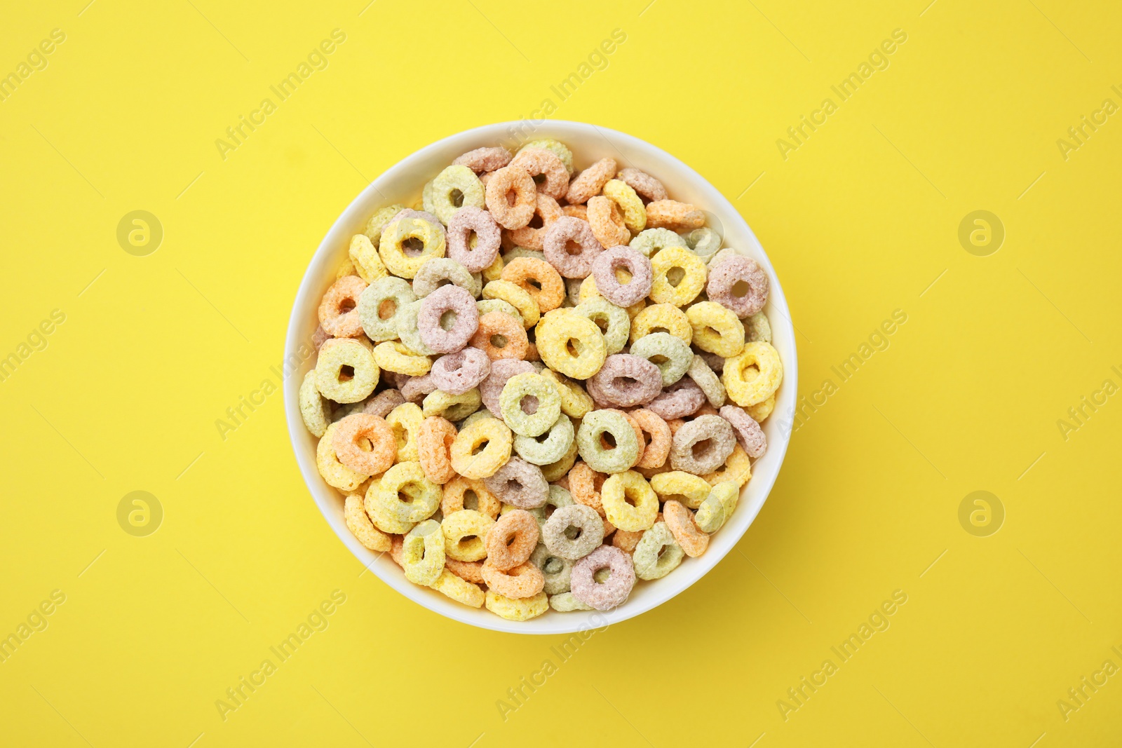 Photo of Tasty cereal rings in bowl on yellow table, top view