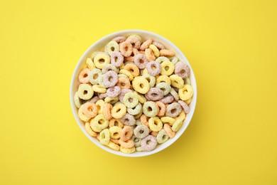 Photo of Tasty cereal rings in bowl on yellow table, top view