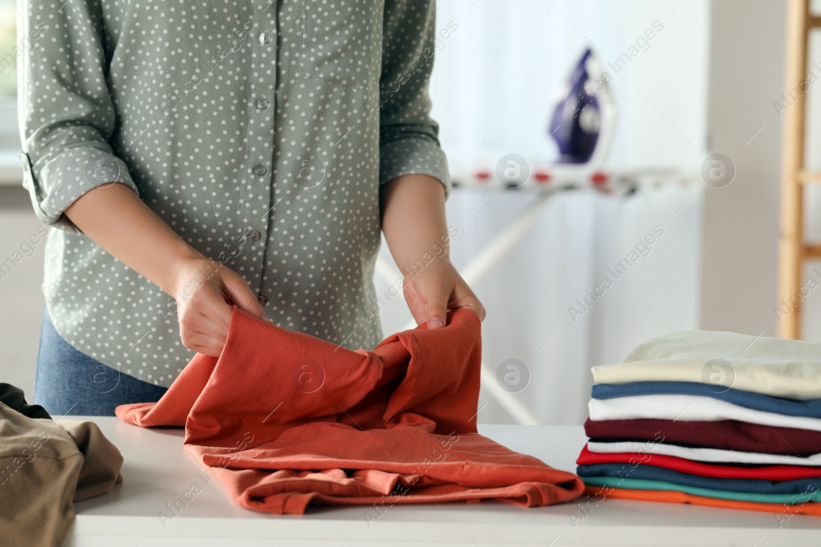 Photo of Woman folding clothes at white table indoors, closeup