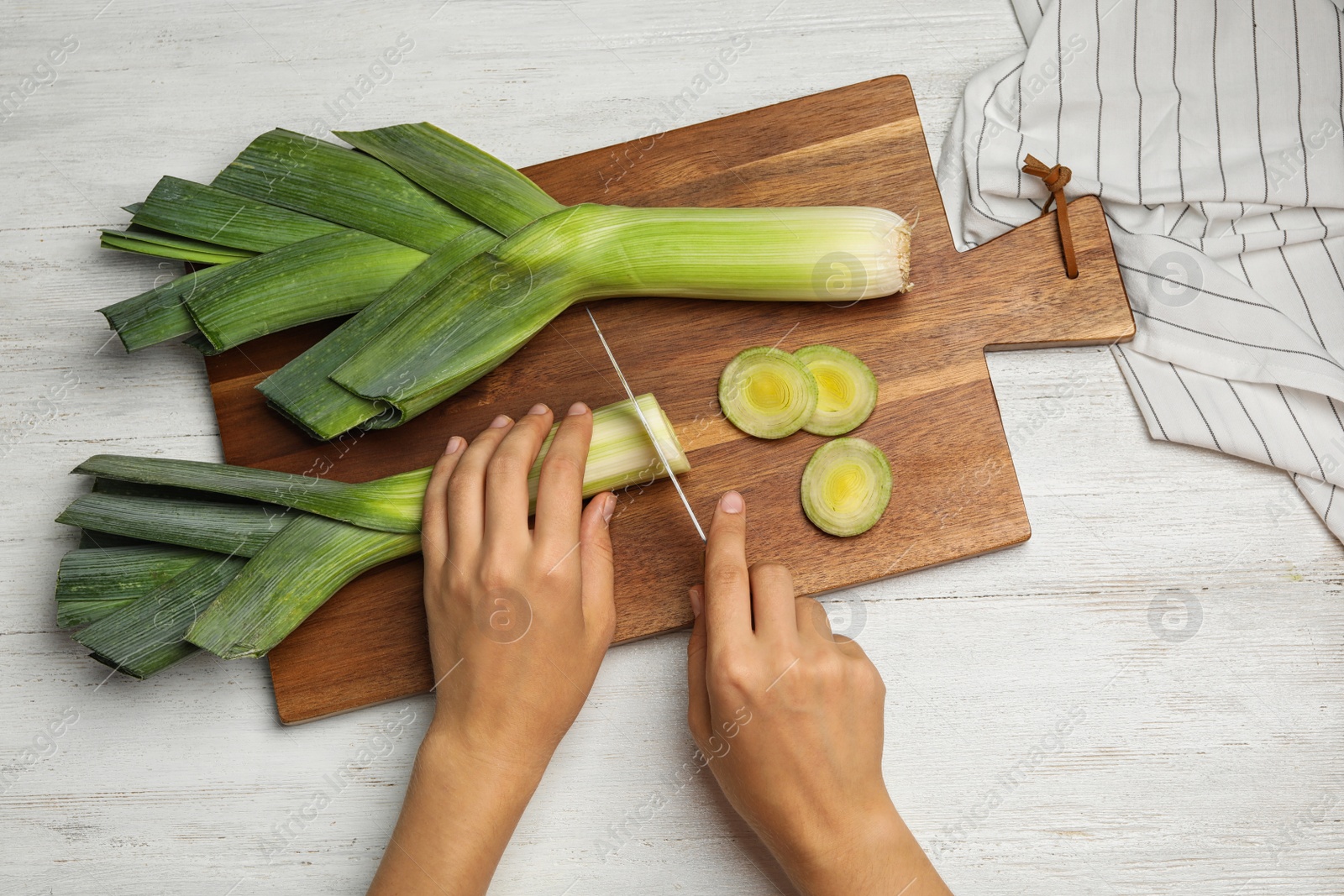 Photo of Woman cutting fresh raw leek on white wooden table, flat lay. Ripe onion