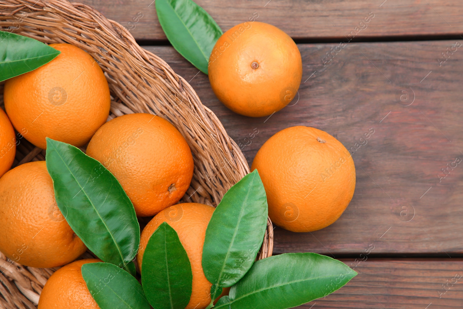 Photo of Wicker basket, ripe juicy oranges and green leaves on wooden table, flat lay
