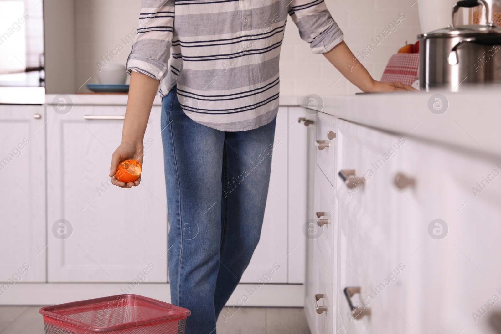 Photo of Woman throwing tangerine peel into trash bin in kitchen, closeup