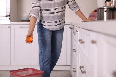 Woman throwing tangerine peel into trash bin in kitchen, closeup