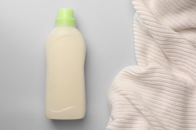 Photo of Bottle of fabric softener and white knitted cloth on light background, flat lay. Space for text