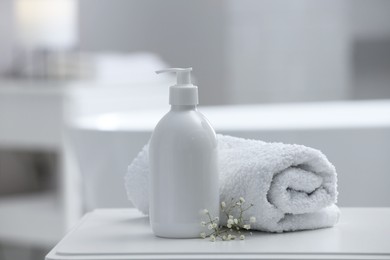 Photo of Bottle of bubble bath, towel and flowers on white table in bathroom