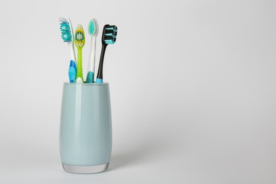 Photo of Different toothbrushes in holder on light grey background. Space for text